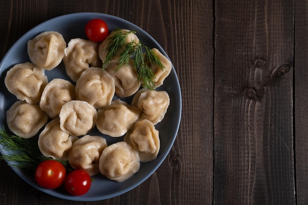 Blauw bord met gekookte zelfgemaakte dumplings met dille en tomaten