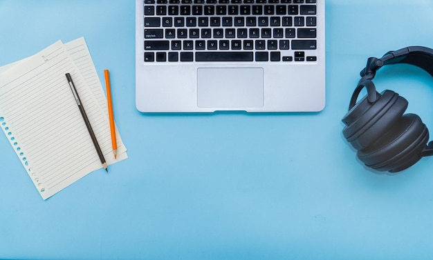 blauw bureau van student met laptop zwarte hoofdtelefoon papieren notitie en potloden negatieve ruimte bovenaanzicht