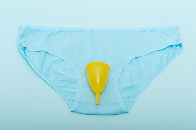 Blauw damesondergoed en een gele menstruatiecup op een blauwe achtergrond gezondheidsconcept voor vrouwen milieuvriendelijk concept geen afvalconcept