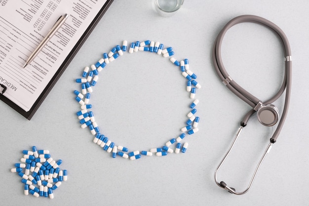 Blauw-witte pillen vormen een grote cirkel op de werkplek met glas water, stethoscoop, document met pen en stapel capsules rond