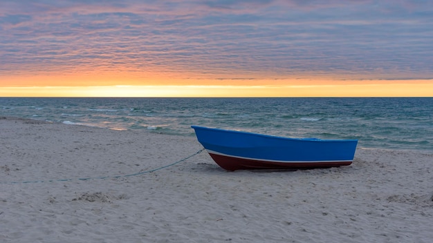 Blauwe boot op het strand bij zonsondergang