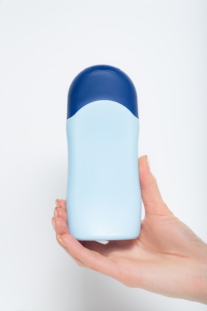Blauwe fles voor cosmetisch product in een vrouwelijke hand. witte achtergrond