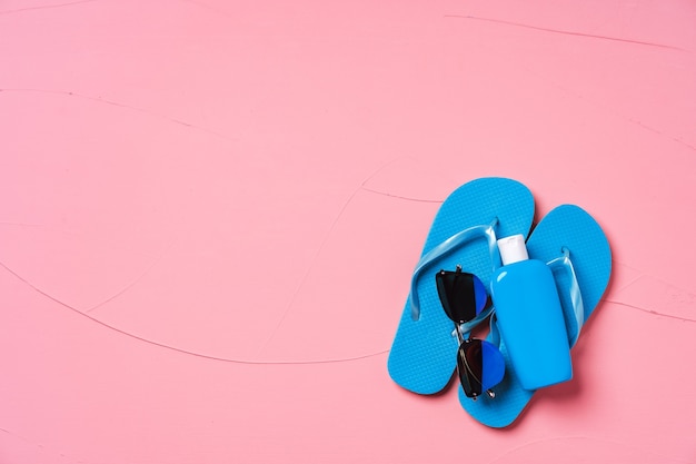 Blauwe flip-flops met zonnebrandcrème en zonnebril op roze, plat leggen