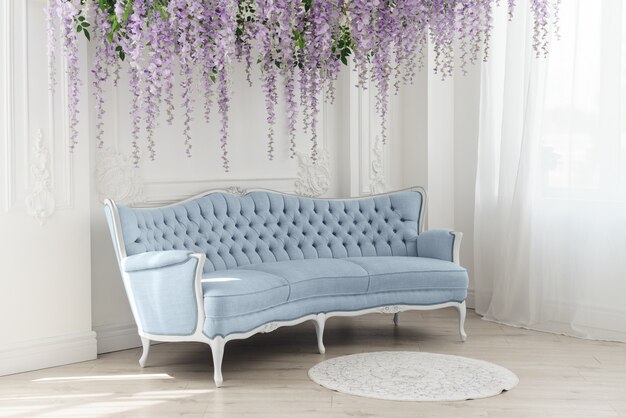 Blauwe Franse bank in witte kamer met decoratieve opgehangen paarse bloemen