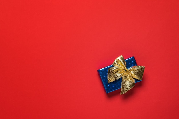 Blauwe geschenkdoos met een gouden strik op een rode achtergrond. Een verrassingsgeschenk.