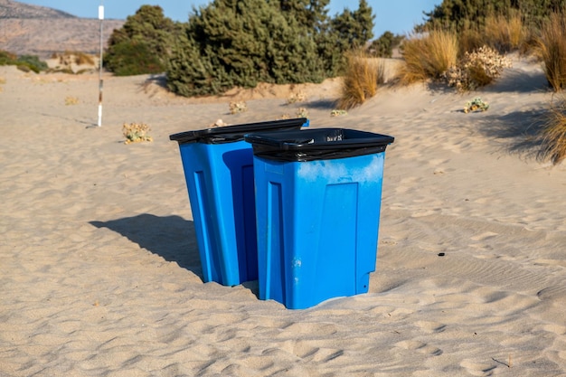 Blauwe grote vuilnisbakken afvalcontainers vuilnisbakken in het midden van de zandige kust Natuur achtergrond