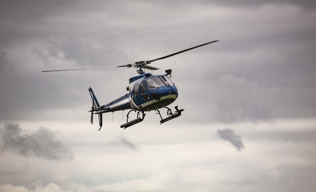 Blauwe helikopter tijdens de vlucht over een grijze lucht