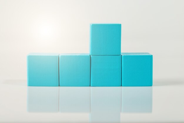 Blauwe houten geometrische vormenkubus die op een witte muur wordt geïsoleerd