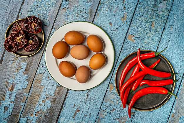 Blauwe houten tafel met kookingrediënten, bruine eieren, hete rode pepers en noras