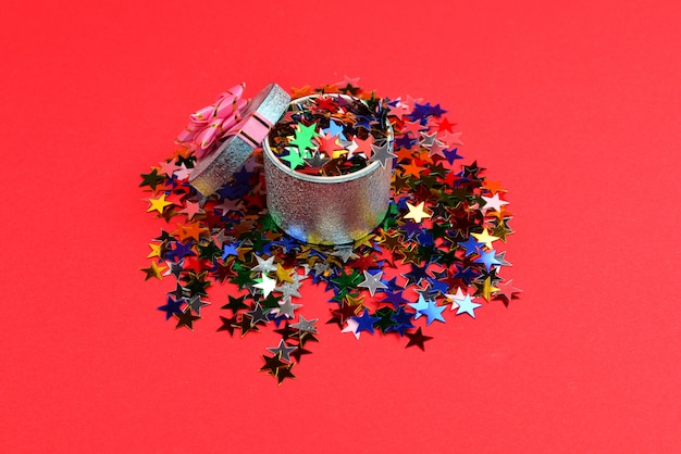 Blauwe huidige doos met roze strik en confetti op een rode achtergrond.
