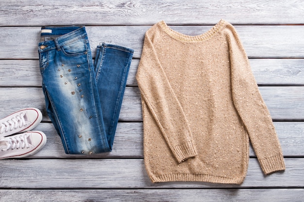 Foto blauwe jeans en beige pullover. sweatshirt op grijze houten achtergrond. lente casual outfit voor dames. beste artikelen in showroom.