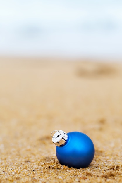 Blauwe kerstbal aan de zandige kust van de oceaan