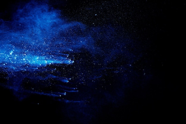 Blauwe kleur poeder explosie wolk op zwarte achtergrond Close-up van blauwe stofdeeltjes spatten