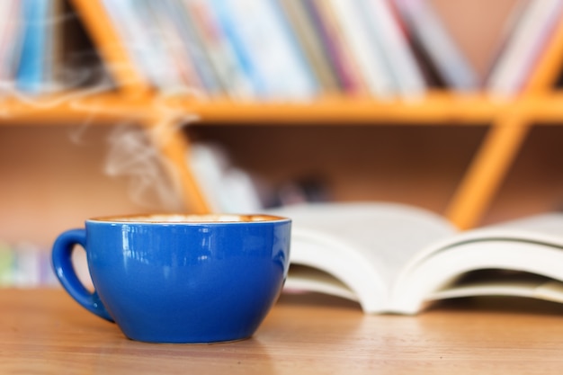 Blauwe koffiekop met boek op tafel.