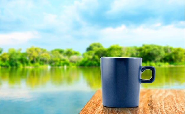 Blauwe koffiekop op houten lijst bij onduidelijk beeldboom en laguneachtergrond