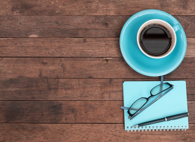 Blauwe koffiekopje, bril, pen en notebook op grunge houten tafel, bovenaanzicht met kopie ruimte