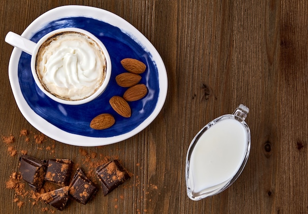 Blauwe kop cappuccino amandelen chocolade en melk in een glazen melkkan