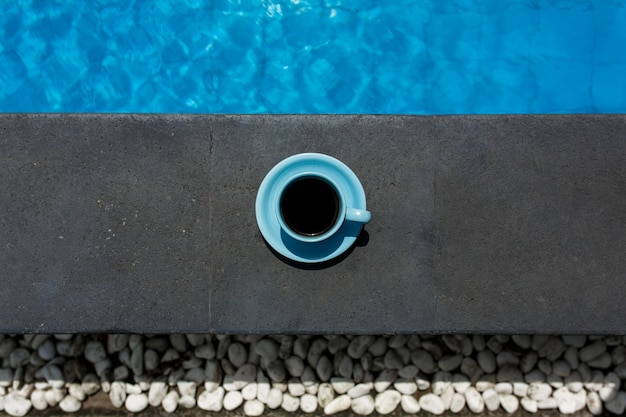 Blauwe kop warme koffie naast het zwembad