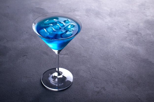 Blauwe koude cocktail in Martiniglas met ijs en duidelijke dauwdruppels