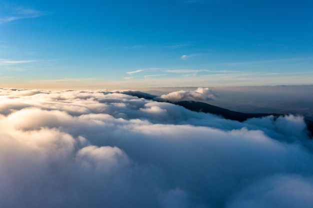 Blauwe lucht boven dikke laag witte pluizige wolken bij feloranje zonsopgang met bergtoppen onder panoramisch uitzicht