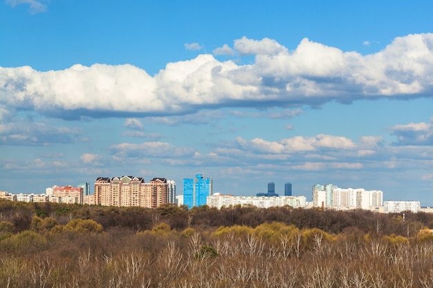 Blauwe lucht met wolken boven stad en bos in het voorjaar