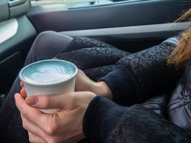 Blauwe matcha latte art in milieuvriendelijke papieren beker Hoofdkleur 2020 jaarconcept Kopje koffie vrouw handen in auto Minimale compositie