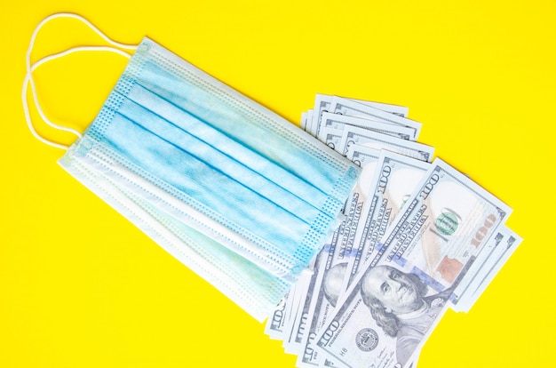 Blauwe medische masker met dollars op een gele achtergrond. Masker en 100 dollarbiljetten op een zwarte achtergrond. Kopieer ruimte. COVID-19