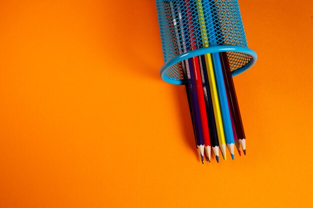 Blauwe metalen emmer met kleurpotloden voor kantoor op een oranje achtergrond