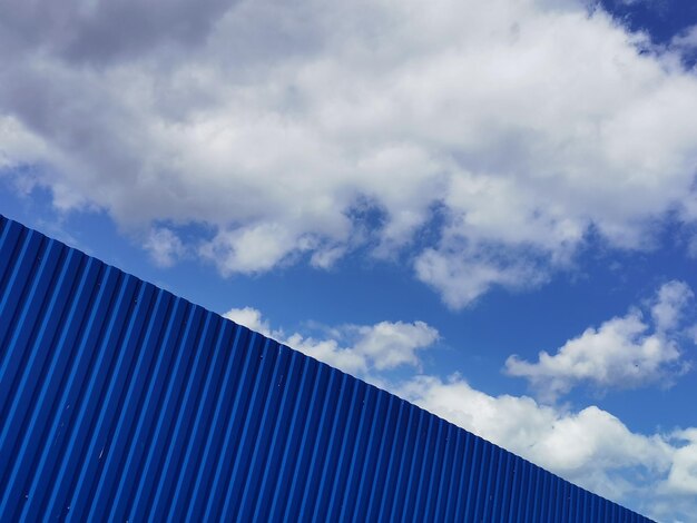 Blauwe metalen plaat tegen blauwe bewolkte lucht Siding Naadloos oppervlak van gegalvaniseerd staal Industriële gebouwmuur gemaakt van gegolfd metalen plaat vlakke achtergrond foto textuur