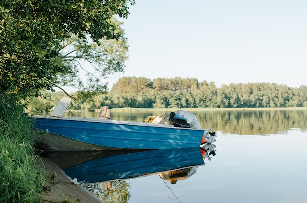 Blauwe motorboot geparkeerd in de buurt van de oever van het meer op een zonnige zomerdag zijaanzicht van een eenvoudige vissersboot op het water