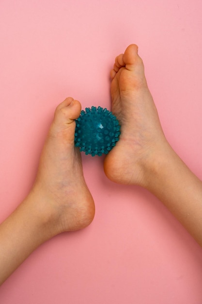 Blauwe naaldbal voor massage en fysiotherapie op een roze achtergrond met de voet van een kind
