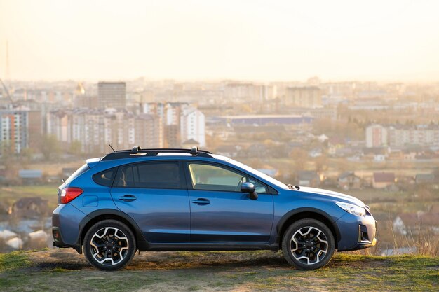 Blauwe off-road auto bij zonsopgang op met gras begroeide heuvel op verre mistige stad landschap achtergrond Extreme reizen op een SUV-auto