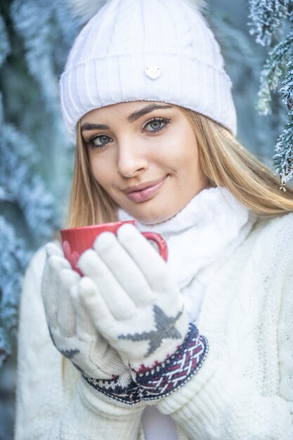 Foto blauwe ogen blond meisje houdt warme drank in handschoenen op een ijskoude winterdag buiten.