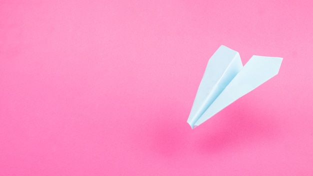 Blauwe origami vliegtuig op roze achtergrond, reizen vluchten kopiëren ruimte.