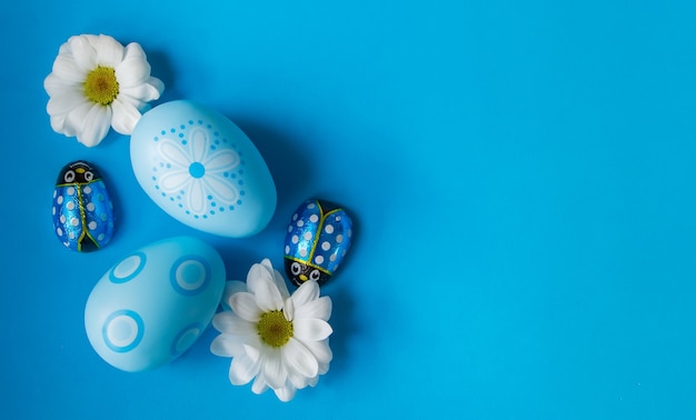 Foto blauwe paaseieren met madeliefjes en chocolade ladybags op blauwe achtergrond