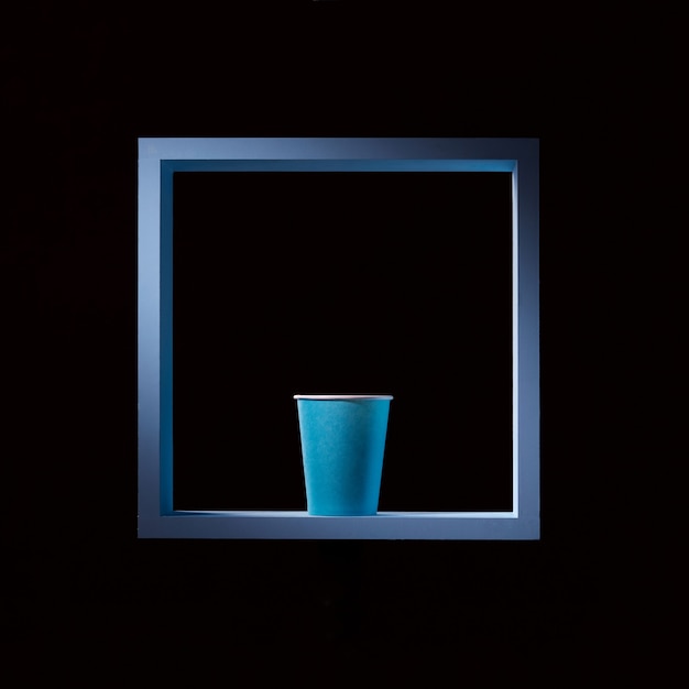 Blauwe papieren beker in een blauw vierkant frame op een zwarte vierkante achtergrond symmetrische centrale compositie