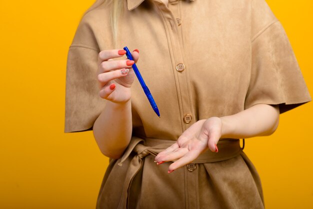 Blauwe pen in vrouwenhand die op geel wordt geïsoleerd.