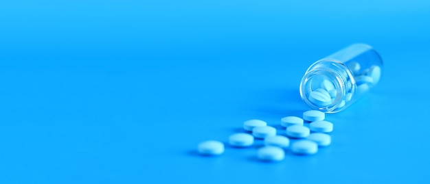 Blauwe pillen uit een glazen fles op een blauwe achtergrond Vitamine B complex zijkant kopieerruimte