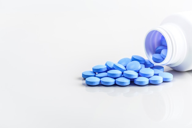 Blauwe pillen zijn verspreid uit een pot op een witte.