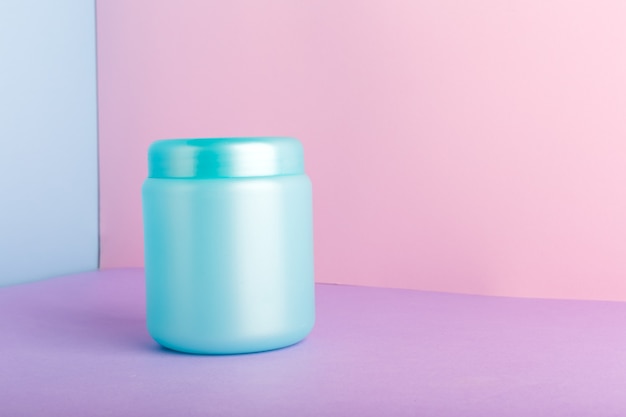Blauwe plastic pot met mock up voor cosmetische producten op een roze achtergrond in kleur met kopie ruimte. Cosmetisch pakket voor haarmasker, conditioner douchegel hygiëneproducten, zelfgemaakte natuurlijke cosmetica.