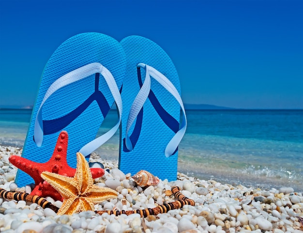 Foto blauwe sandalen en zeesterren op witte kiezelstenen aan de kust