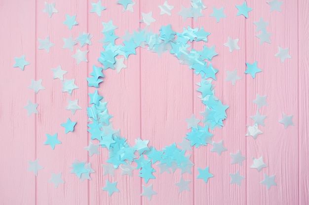 Foto blauwe sterrenconfettien op een roze houten achtergrond met rond kader