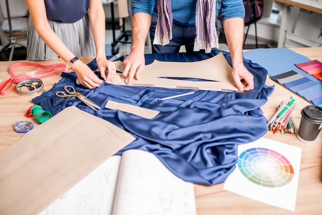 Blauwe stof snijden op de tafel vol kleermakersgereedschap. Close-up van de handen en stof zonder gezicht