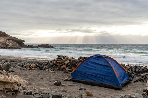 Foto blauwe tent op een strand tegen de oceaan en de zonnestraal die door de wolken komtfuerteventuracanarische eilanden