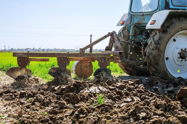 Blauwe tractor die land met ploeg voorbereidt om te zaaien