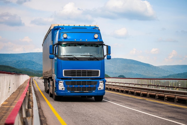 Foto blauwe vrachtwagen op een weg die door een brug beweegt.