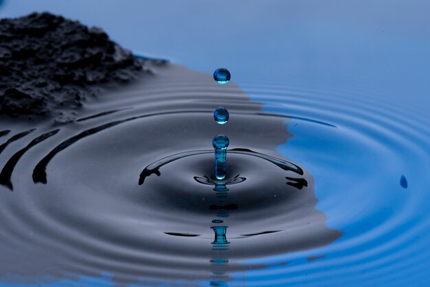 Foto blauwe waterdruppels bevroren in de lucht en vormen rimpelingen op het vloeibare oppervlak