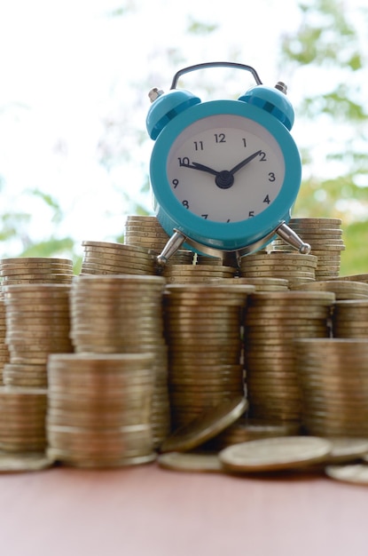 Foto blauwe wekker op grote hoeveelheid glanzende oekraïense oude 1 hryvnia munt stapels close-up op wazig groene bomen achtergrond het concept van financiële planning en business time management