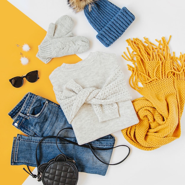 Blauwe wintermuts met jeans, trui, handtas en gele sjaal op witte achtergrond. Stijlvolle herfst- of winteroutfit voor dames. Trendy kledingcollage. Plat lag, bovenaanzicht.