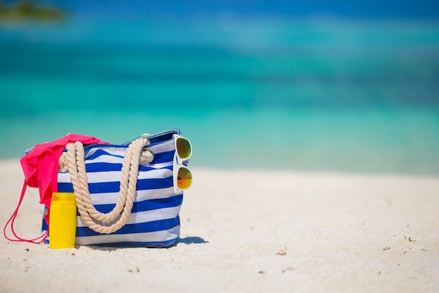 Blauwe zak, zwempak, zonnebril en suncream op wit strand